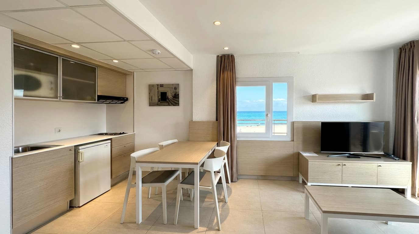 Salón con cocina de un apartamento del Aparthotel Acualandia en Peñíscola, con la playa asomando por la ventana como si fuera un cuadro