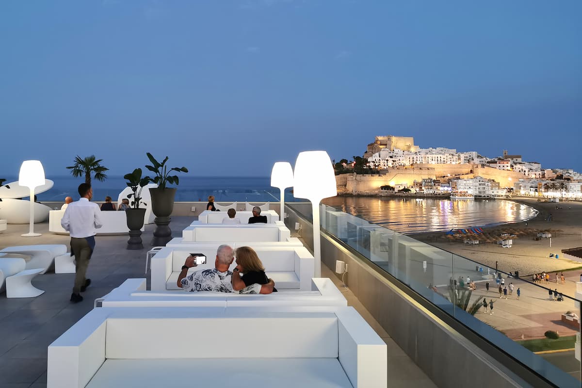 Pareja disfrutando del atardecer en la terraza panorámica con vistas al casco antiguo iluminado y la playa