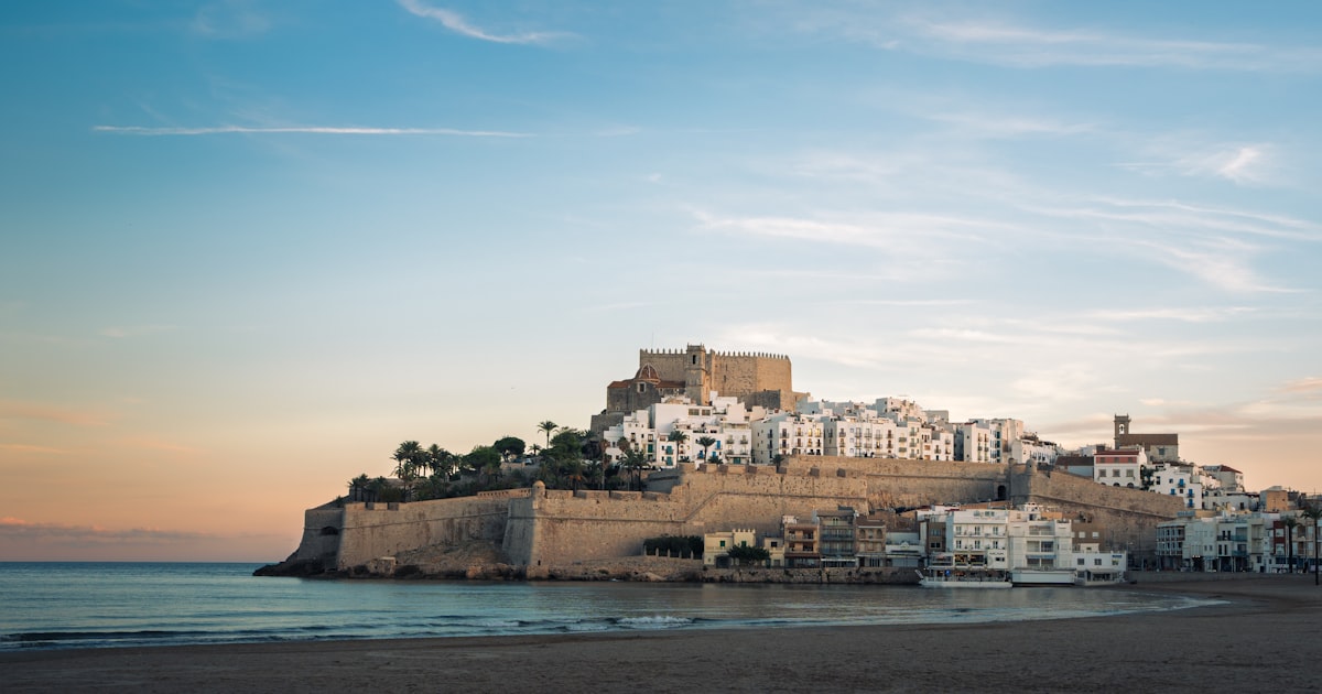 El castillo de Peñíscola sobre el peñón amurallado junto al mar Mediterráneo al atardecer, con la playa en primer plano